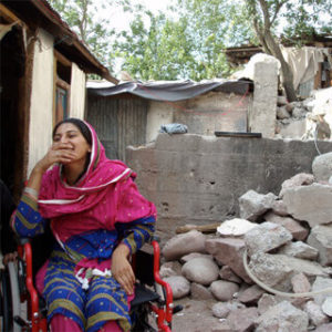 woman in wheelchair by a broken-down building